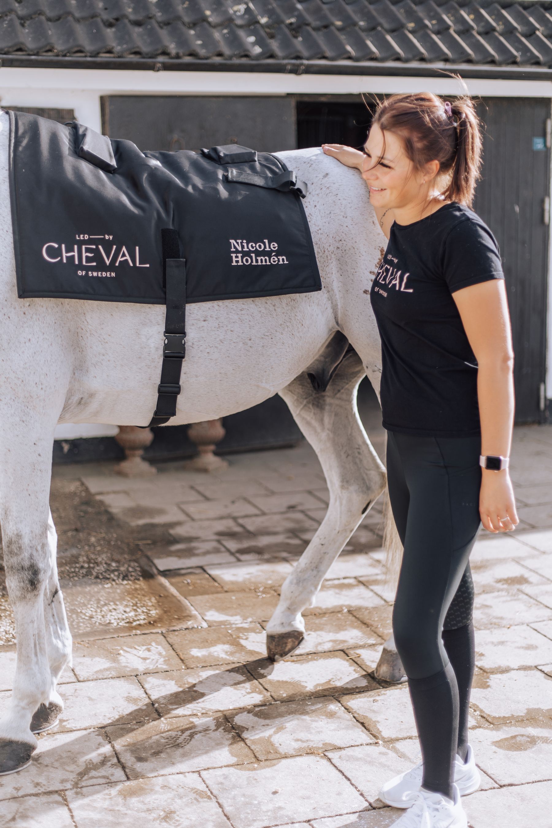 Nicole Holmén with her grey horse in the stable yard, the horse wearing an LED by CHEVAL rug